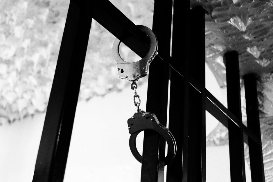 Black and white photo of handcuffs on steel bars, depicting confinement theme.
